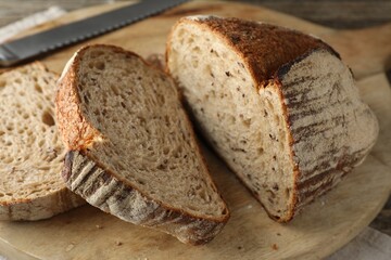 Cut loaf of fresh bread and knife on wooden table, closeup