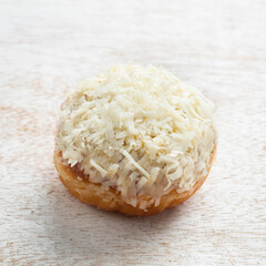 A sweet cheese donut lies on a rustic wooden surface, topped generously with freshly shredded coconut, inviting indulgence