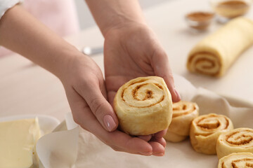 Woman putting cinnamon roll into baking dish at table, closeup