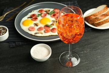 Tasty brunch. Aperol cocktail, delicious fried eggs with sausage served on black table, closeup