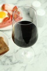 Tasty brunch. Glass of red wine, fried egg and sausage on white marble table, closeup
