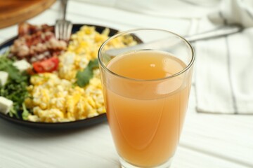 Tasty brunch. Glass of apple juice and scrambled eggs with bacon served on white wooden table, closeup