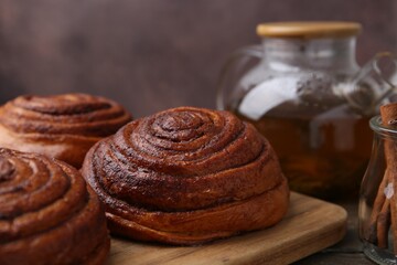 Delicious cinnamon rolls on wooden table against brown background, closeup