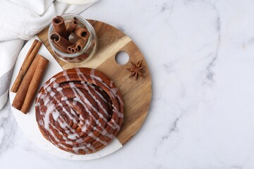 Tasty cinnamon roll with cream and spices on white marble table, top view. Space for text