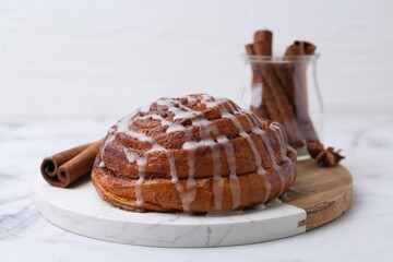 Tasty cinnamon roll with cream and spices on white table, closeup