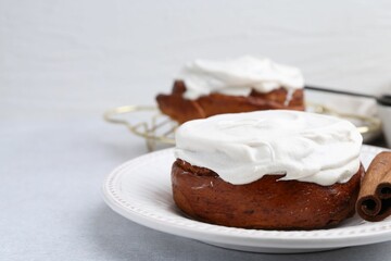 Tasty cinnamon rolls with cream and stick on light table, closeup. Space for text