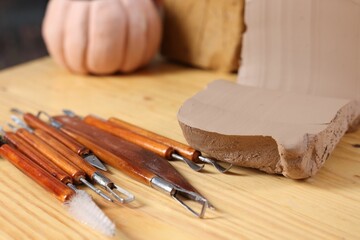 Set of different crafting tools and pieces of clay on wooden table, closeup