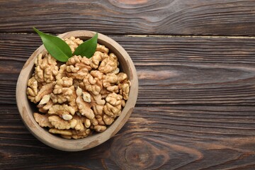 Peeled walnuts and green leaves in bowl on wooden table, top view. Space for text