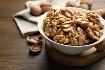 Peeled walnuts in bowl on wooden table, closeup. Space for text