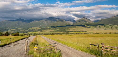 Low lying clouds cover the beautiful mountain range in Wyoming with a dirt road leading off into the distance in a Panoramic Image