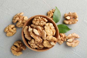Peeled walnuts in bowl and green leaves on table, flat lay