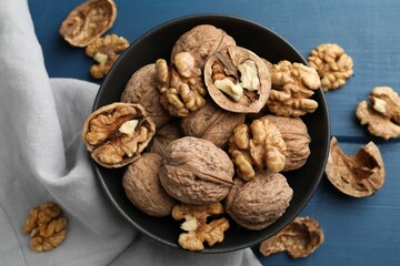 Fresh walnuts in bowl on blue wooden table, flat lay