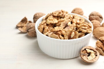 Peeled walnuts in bowl on light wooden table, closeup. Space for text