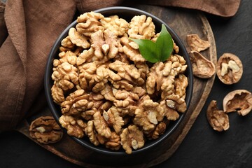 Fresh ripe walnuts in bowl and shells on black table, top view