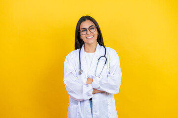 Young brunette doctor woman wearing stethoscope standing over isolated yellow background with a happy face standing and smiling with a confident smile showing teeth with arms crossed