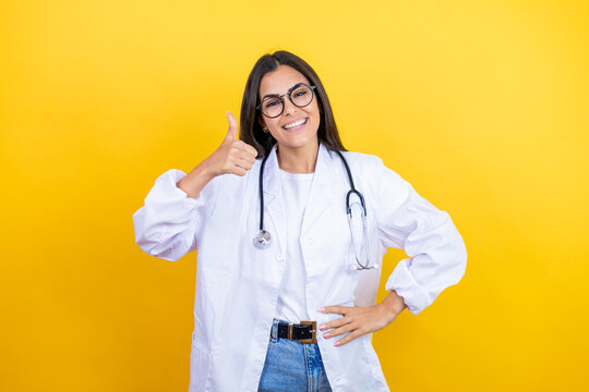 Young doctor woman wearing stethoscope standing over isolated yellow background success sign doing positive gesture with hand, thumb up smiling and happy. cheerful expression and winner gesture.
