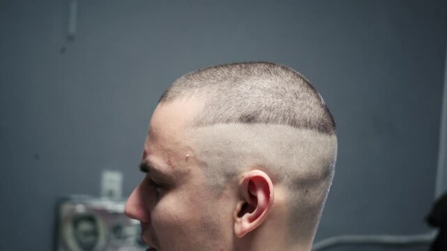 young guy cuts his hair and makes a short bald haircut. Master barber in a barbershop makes a haircut to a client close-up. Skinhead man of criminal appearance shaves his head with a machine