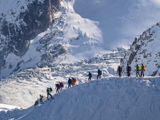 Paragliders with large backpacks with a parachute inside descend a steep snowy slope from the...