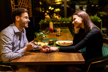 Loving boyfriend gifts a red rose to his girlfriend on a romantic dinner date.
