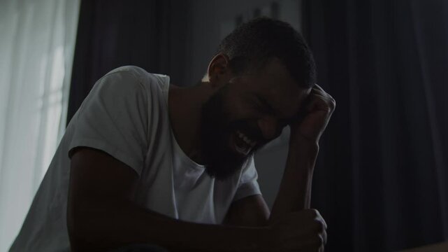 African American man screams expressing despair in bedroom