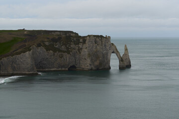 The winter landscape at Etretat is calm and inviting, with grey skies and smooth waves reflecting the tranquility.
