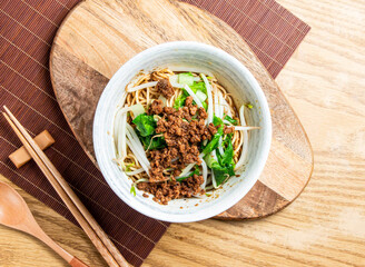 Dan Dan Noodles with Ground Pork in sesame sauce served in bowl with chopsticks and spoon isolated on wooden board side view of taiwan food