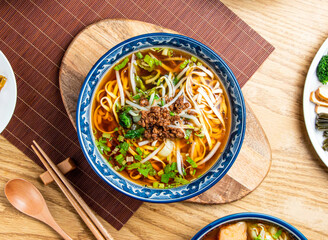 Taiwanese Noodle Soup topping with mince meat served in bowl with chopsticks and spoon isolated on wooden board top view of taiwan food