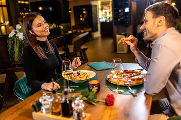 Happy couple on a dinner date in a fancy restaurant. They eat delicious pizza and pasta.