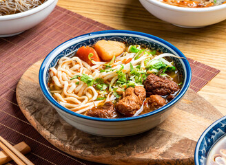 Vegetarian Beef Noodle Soup topped with green onion, carrot, and coriander served in bowl with chopsticks and spoon isolated on wooden board side view of taiwan food