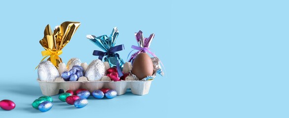 Holder with chocolate Easter eggs on light blue background with space for text