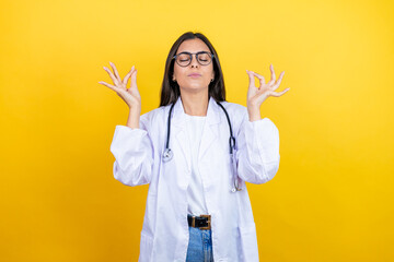 Young brunette doctor woman wearing stethoscope standing over isolated yellow background relax and smiling with eyes closed doing meditation gesture with fingers