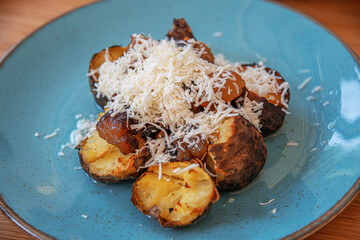 A plate of roasted potatoes with crispy, golden-brown edges is generously topped with freshly grated cheese.