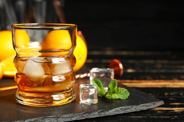 Glass of rum with ice cubes on dark wooden background