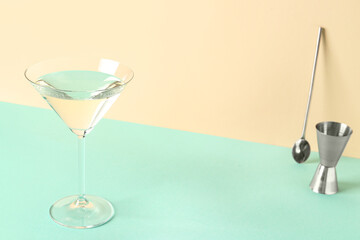 Glass of martini, bar spoon and jigger on color background