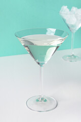 Glass of martini and ice on color background