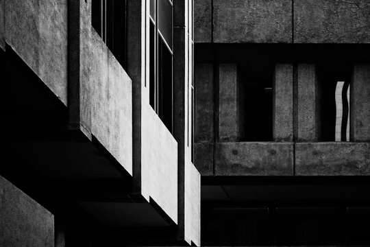Black and white fine art photography. High contrast abstraction of two concrete buildings built in brutalist architectural style. Juxtaposition of sunlit diagonal and straight blocks in shadow. 