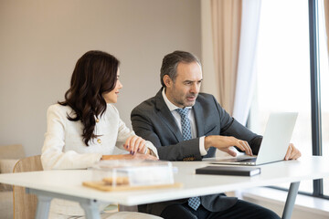 In a contemporary office, a man and woman analyze data together on a laptop, emphasizing collaboration and the importance of teamwork in business decision-making.