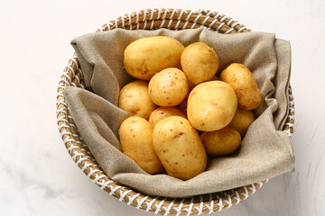 Wicker bowl with raw baby potatoes on white background