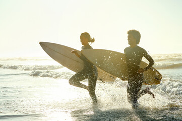 Sunset, running and couple in the ocean water with surfboards to practice surfing while on vacation. Nature, sports and young man and woman surfers in the sea while on a beach holiday in Hawaii.