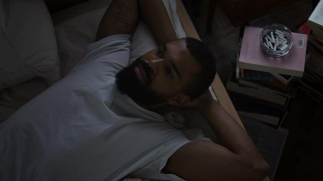 African American man reclines on bed staring at ceiling