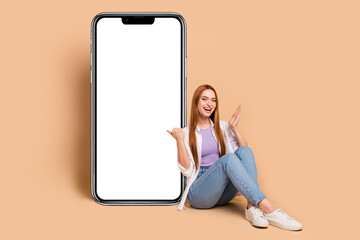 Full size photo of overjoyed woman wear white cardigan sit directing at smartphone display empty...