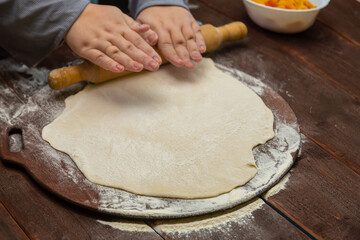 Women's hands roll out dough with a rolling pin on a wooden baking table