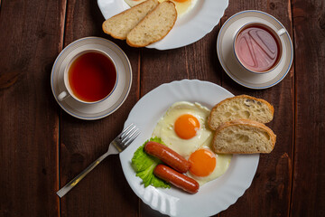 Breakfast fried eggs with sausages white bread and tea in a cup on a wooden table