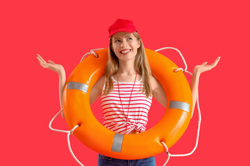 Young female lifeguard in cap with rescue ring and whistle on red background