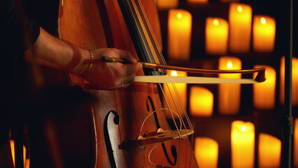 Close-up of a musician playing the double bass on a stage surrounded by candles.