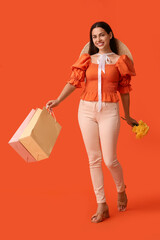 Beautiful young happy woman with bouquet of flowers and shopping bags on orange background