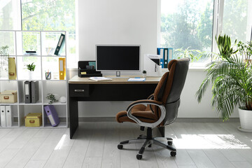 Interior of office with workplace, armchair, modern computer and shelving unit
