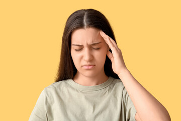 Beautiful young woman suffering from headache on yellow background
