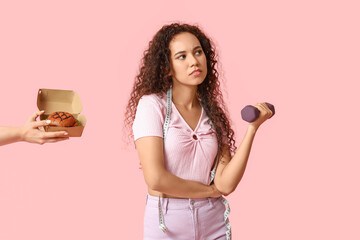 Young African-American woman with measuring tape and dumbbell turn away from hand with burger on...