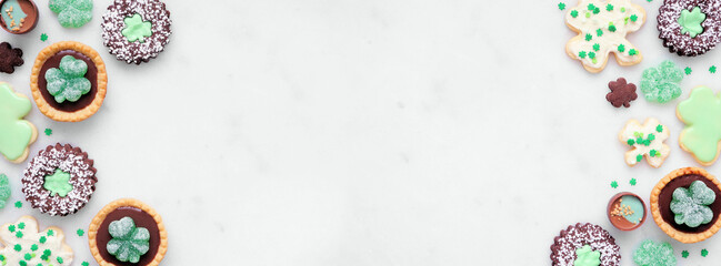 St Patricks Day dessert double border over a white stone banner background. Shamrock and green cookies, tarts, chocolate and candy. Top down view. Copy space.